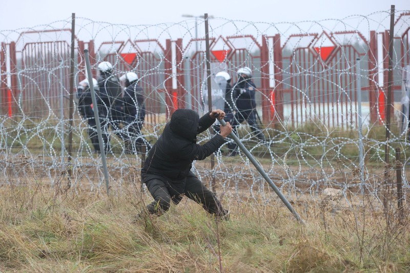 Polish law enforcement officers use water cannons, as migrants carry a log towards a fence at Kuznica - Bruzgi checkpoint, Poland, November 16, 2021. Policja Podlaska/Handout via REUTERS NO RESALES. NO ARCHIVES. MANDATORY CREDIT. THIS IMAGE HAS BEEN SUPPLIED BY A THIRD PARTY.