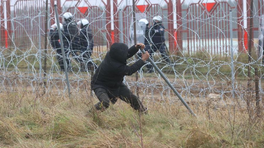 Polish law enforcement officers use water cannons, as migrants carry a log towards a fence at Kuznica - Bruzgi checkpoint, Poland, November 16, 2021. Policja Podlaska/Handout via REUTERS NO RESALES. NO ARCHIVES. MANDATORY CREDIT. THIS IMAGE HAS BEEN SUPPLIED BY A THIRD PARTY.