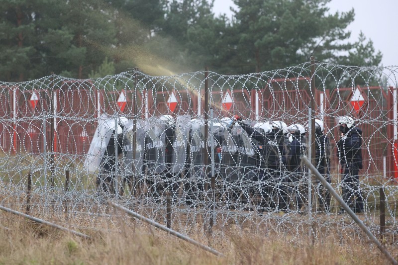 Polish law enforcement officers use water cannons, as migrants carry a log towards a fence at Kuznica - Bruzgi checkpoint, Poland, November 16, 2021. Policja Podlaska/Handout via REUTERS NO RESALES. NO ARCHIVES. MANDATORY CREDIT. THIS IMAGE HAS BEEN SUPPLIED BY A THIRD PARTY.