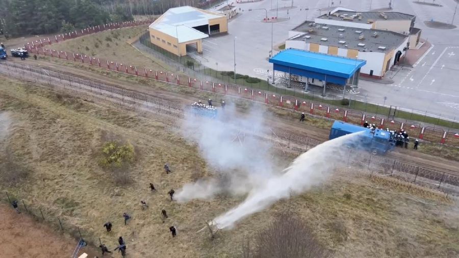 Polish law enforcement officers use water cannons, as migrants carry a log towards a fence at Kuznica - Bruzgi checkpoint, Poland, November 16, 2021. Policja Podlaska/Handout via REUTERS NO RESALES. NO ARCHIVES. MANDATORY CREDIT. THIS IMAGE HAS BEEN SUPPLIED BY A THIRD PARTY.