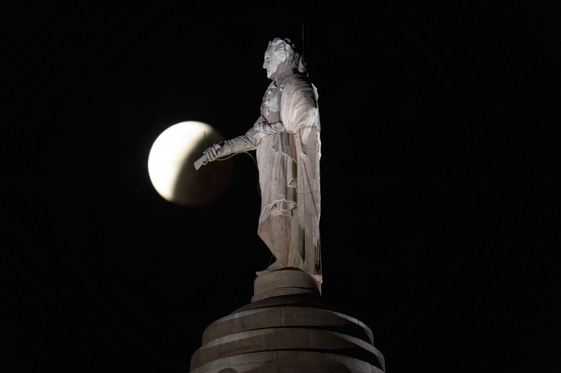 Orang-orang menyaksikan gerhana bulan parsial di atas Catania di Piazza Universita, Italia (19/11/2021). (REUTERS/Antonio Parrinello)