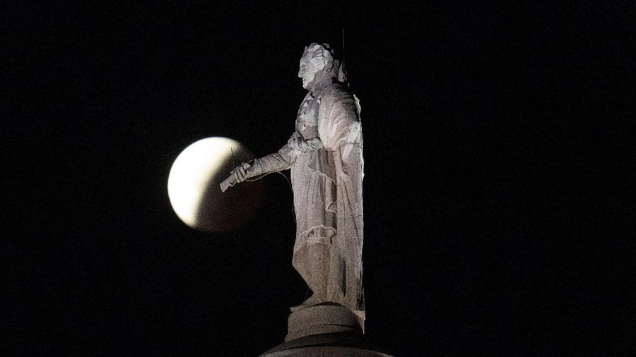 Orang-orang menyaksikan gerhana bulan parsial di atas Catania di Piazza Universita, Italia (19/11/2021). (REUTERS/Antonio Parrinello)