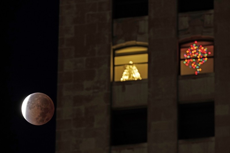 Orang-orang menyaksikan gerhana bulan parsial di atas Catania di Piazza Universita, Italia (19/11/2021). (REUTERS/Antonio Parrinello)