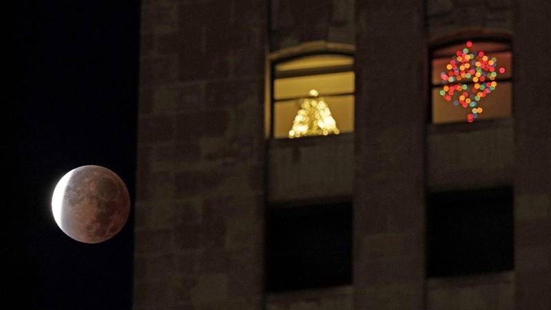 Orang-orang menyaksikan gerhana bulan parsial di atas Catania di Piazza Universita, Italia (19/11/2021). (REUTERS/Antonio Parrinello)