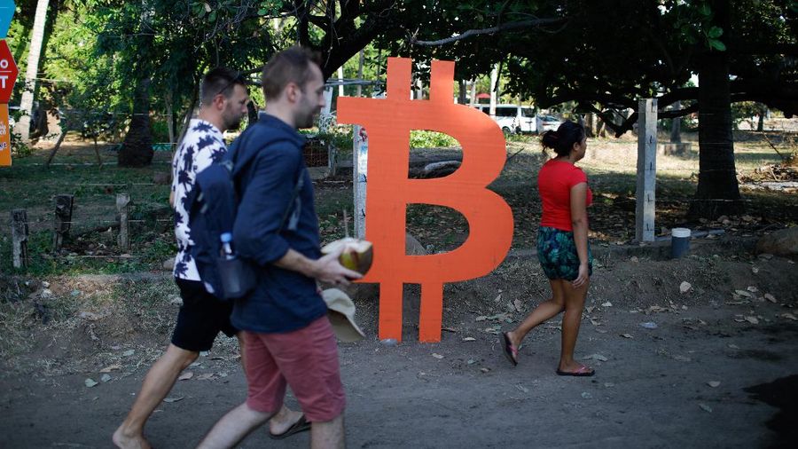 People walk by a Bitcoin sign during a meet up between local bitcoin users and foreigners at the closing of Adopting Bitcoin - A Lightning Summit, at El Zonte Beach, in Chiltiupan, El Salvador November 18, 2021. REUTERS/Jose Cabezas