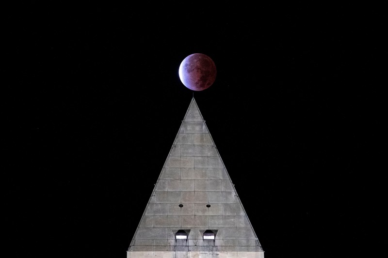 Gerhana bulan parsial atau Bulan darah di atas Catania di Piazza Universita, Italia Orang-orang menyaksikan gerhana bulan parsial di atas Catania di Piazza Universita, Italia (19/11/2021). (REUTERS/Antonio Parrinello)
