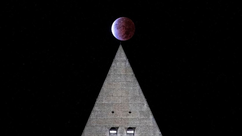 Orang-orang menyaksikan gerhana bulan parsial di atas Catania di Piazza Universita, Italia (19/11/2021). (REUTERS/Antonio Parrinello)