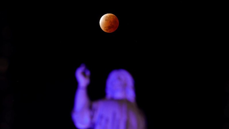 Orang-orang menyaksikan gerhana bulan parsial di atas Catania di Piazza Universita, Italia (19/11/2021). (REUTERS/Antonio Parrinello)
