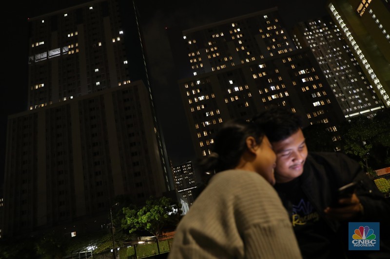 Sejumlah warga berbincang dengan latar belakang Gedung Wisma Atlet, Kemayoran yang gelap, Selasa (23/11/2021). Jumlah pasien di Rumah Sakit Darurat Covid-19 (RSDC) Wisma Atlet, Kemayoran, Jakarta, terus berkurang dalam beberapa waktu terakhir.
Dari pantauan CNBC Indonesia dilokasi hanya beberapa keluarga yang datang hilir mudik untuk menjemput keluarga pasien Covid-19 yang memang sudah terindikasi negatif dan diizinkan untuk pulang. 
Menurut penjaga pintu darurat yang tidak ingin disebutkan namanya mengatakan 