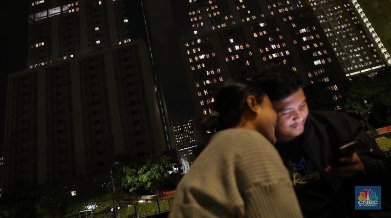 Sejumlah warga berbincang dengan latar belakang Gedung Wisma Atlet, Kemayoran yang gelap, Selasa (23/11/2021). Jumlah pasien di Rumah Sakit Darurat Covid-19 (RSDC) Wisma Atlet, Kemayoran, Jakarta, terus berkurang dalam beberapa waktu terakhir.
Dari pantauan CNBC Indonesia dilokasi hanya beberapa keluarga yang datang hilir mudik untuk menjemput keluarga pasien Covid-19 yang memang sudah terindikasi negatif dan diizinkan untuk pulang. 
Menurut penjaga pintu darurat yang tidak ingin disebutkan namanya mengatakan 