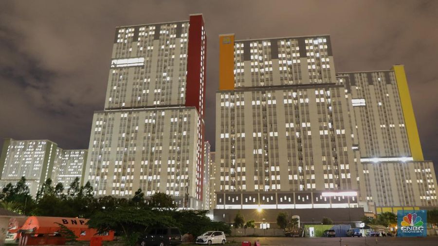 Sejumlah warga berbincang dengan latar belakang Gedung Wisma Atlet, Kemayoran yang gelap, Selasa (23/11/2021). Jumlah pasien di Rumah Sakit Darurat Covid-19 (RSDC) Wisma Atlet, Kemayoran, Jakarta, terus berkurang dalam beberapa waktu terakhir.
Dari pantauan CNBC Indonesia dilokasi hanya beberapa keluarga yang datang hilir mudik untuk menjemput keluarga pasien Covid-19 yang memang sudah terindikasi negatif dan diizinkan untuk pulang. 
Menurut penjaga pintu darurat yang tidak ingin disebutkan namanya mengatakan 