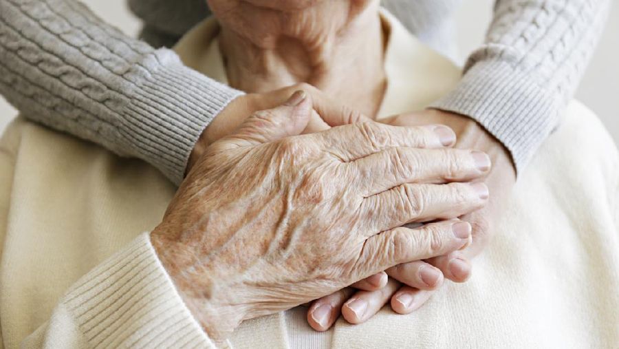 Mature female in elderly care facility gets help from hospital personnel nurse. Senior woman, aged wrinkled skin & hands of her care giver. Grand mother everyday life. Background, copy space, close up