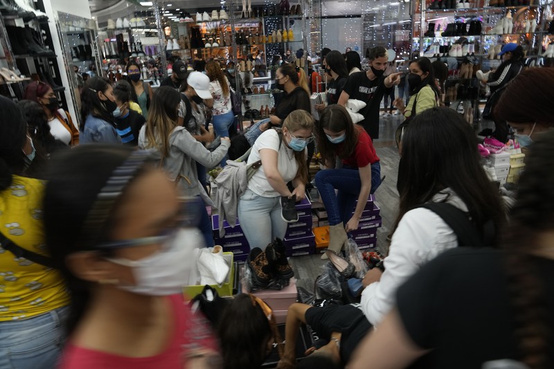 Shoppers, wearing protective face masks, line up to enter the Sambil Mall, in Caracas, Venezuela, Friday, Nov. 26, 2021.  At malls and few stores, Venezuelans are taking the opportunity to buy clothes and other articles with generous Black Friday discounts. (AP Photo/Ariana Cubillos)