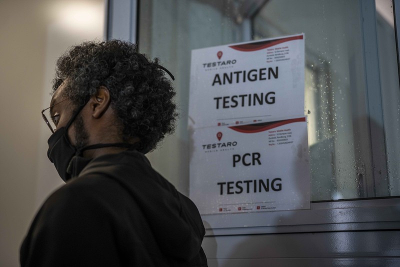 A petrol attendant stands next to a newspaper headline in Pretoria, South Africa, Saturday, Nov. 27, 2021. As the world grapples with the emergence of the new variant of COVID-19, scientists in South Africa — where omicron was first identified — are scrambling to combat its spread across the country. (AP Photo/Denis Farrell)