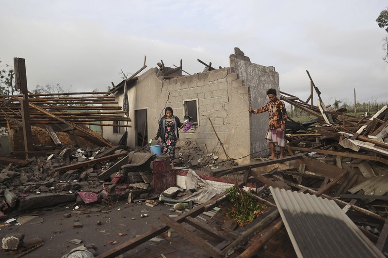 Kondisi Rumah Warga Usai Erupsi Gunung Semeru (5/12/2021) A man brings his buffaloes for evacuation past houses covered with ash following an eruption of Mount Semeru, seen in the background, in Lumajang, East Java, Indonesia, Sunday, Dec. 5, 2021. The highest volcano on Indonesia’s most densely populated island of Java spewed thick columns of ash, searing gas and lava down its slopes in a sudden eruption triggered by heavy rains on Saturday. (AP Photo/Trisnadi)