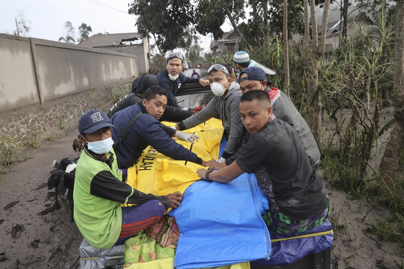 Kondisi Rumah Warga Usai Erupsi Gunung Semeru (5/12/2021) A man brings his buffaloes for evacuation past houses covered with ash following an eruption of Mount Semeru, seen in the background, in Lumajang, East Java, Indonesia, Sunday, Dec. 5, 2021. The highest volcano on Indonesia’s most densely populated island of Java spewed thick columns of ash, searing gas and lava down its slopes in a sudden eruption triggered by heavy rains on Saturday. (AP Photo/Trisnadi)