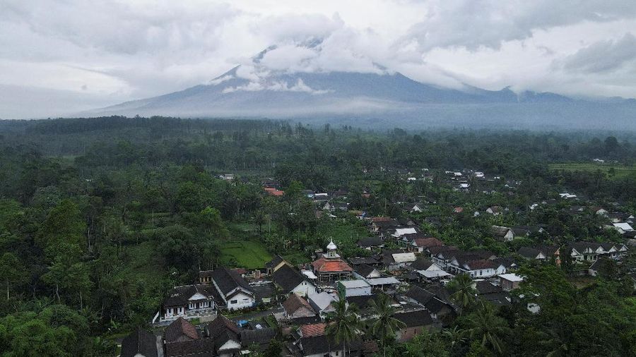 Herni, a 44-year-old local resident, sweeps ash on the ground as Mount Semeru volcano continues to spew ash and smoke in the background, at the Volcano Observatory in Candipuro district, Lumajang regency, Indonesia, December 6, 2021. REUTERS/Willy Kurniawan