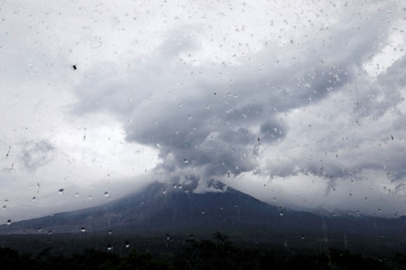 Herni, a 44-year-old local resident, sweeps ash on the ground as Mount Semeru volcano continues to spew ash and smoke in the background, at the Volcano Observatory in Candipuro district, Lumajang regency, Indonesia, December 6, 2021. REUTERS/Willy Kurniawan