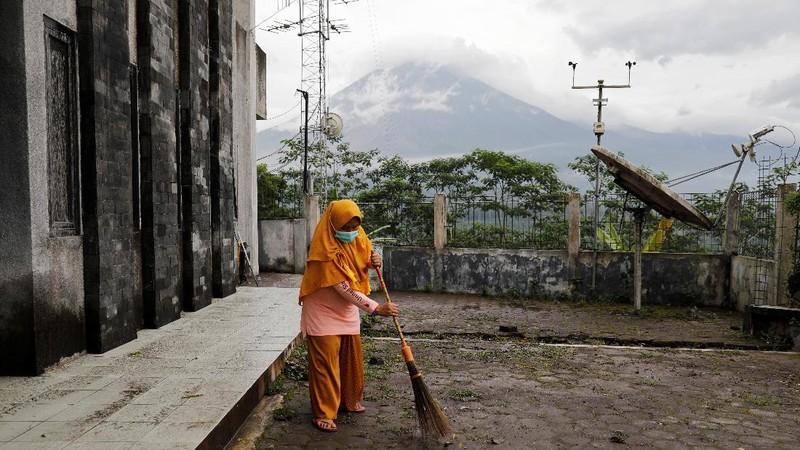 Herni, a 44-year-old local resident, sweeps ash on the ground as Mount Semeru volcano continues to spew ash and smoke in the background, at the Volcano Observatory in Candipuro district, Lumajang regency, Indonesia, December 6, 2021. REUTERS/Willy Kurniawan