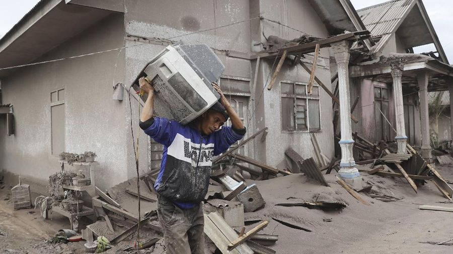 A man carries a television as he evacuates to a safer place following the eruption of Mount Semeru in Lumajang district, East Java province, Indonesia, Monday, Dec. 6, 2021. The highest volcano on Java island spewed thick columns of ash into the sky in a sudden eruption Saturday triggered by heavy rains. Villages and nearby towns were blanketed and several hamlets buried under tons of mud from volcanic debris. (AP Photo/Trisnadi)