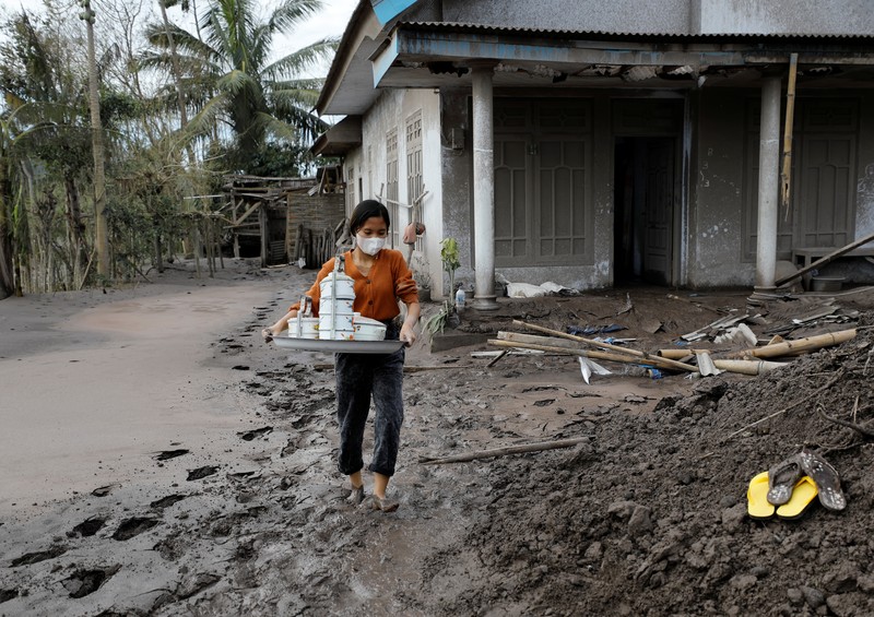 Locals transport a mattress on a motorcycle as Mount Semeru volcano continues to spew ash and smoke in the background following an eruption, in Gunung Sawur, Candipuro, Indonesia December 7, 2021. REUTERS/Willy Kurniawan     TPX IMAGES OF THE DAY