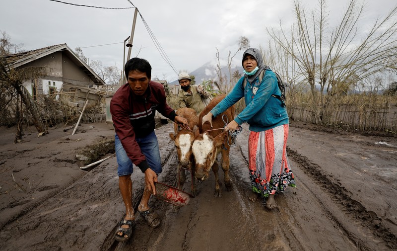 Locals transport a mattress on a motorcycle as Mount Semeru volcano continues to spew ash and smoke in the background following an eruption, in Gunung Sawur, Candipuro, Indonesia December 7, 2021. REUTERS/Willy Kurniawan     TPX IMAGES OF THE DAY