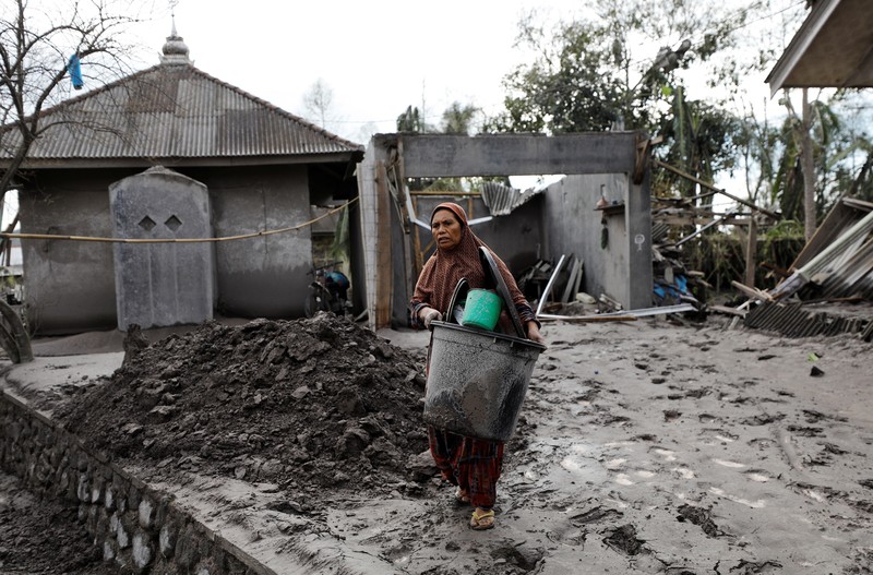 INDONESIA-VOLCANO/ Locals transport a mattress on a motorcycle as Mount Semeru volcano continues to spew ash and smoke in the background following an eruption, in Gunung Sawur, Candipuro, Indonesia December 7, 2021. REUTERS/Willy Kurniawan TPX IMAGES OF THE DAY