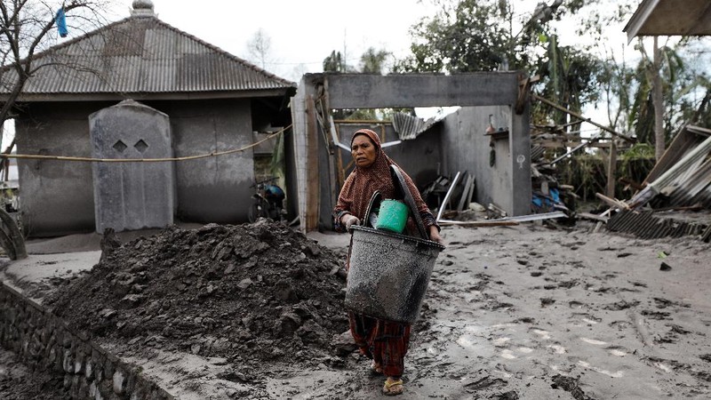 Locals transport a mattress on a motorcycle as Mount Semeru volcano continues to spew ash and smoke in the background following an eruption, in Gunung Sawur, Candipuro, Indonesia December 7, 2021. REUTERS/Willy Kurniawan     TPX IMAGES OF THE DAY