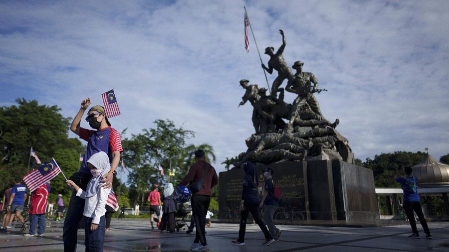Visitors pose with Malaysian national flags for a photo in front of the National Monument during the 64th National Day celebrations to commemorate independence of Malaysia from British colonial rule, in Kuala Lumpur, Malaysia, Tuesday, Aug. 31, 2021. (AP Photo/Vincent Thian)