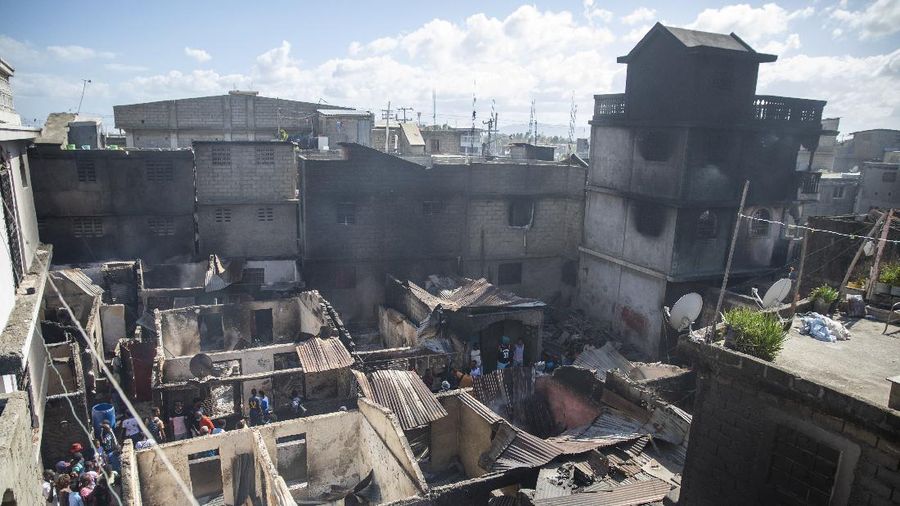 Warga berdiri di tengah rumah yang rusak akibat truk bensin terbalik dan meledak di Cap-Hatien, Haiti, Selasa (14/12/2021). Ledakan itu menghanguskan mobil dan rumah, menewaskan lebih dari 50 orang dan melukai puluhan lainnya. (AP/Joseph Odelyn)