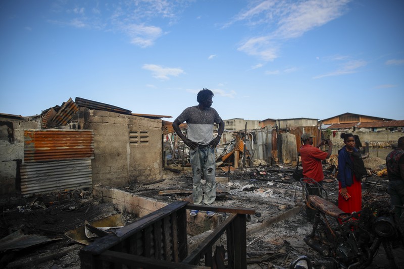 Warga berdiri di tengah rumah yang rusak akibat truk bensin terbalik dan meledak di Cap-Hatien, Haiti, Selasa (14/12/2021). Ledakan itu menghanguskan mobil dan rumah, menewaskan lebih dari 50 orang dan melukai puluhan lainnya. (AP/Joseph Odelyn)