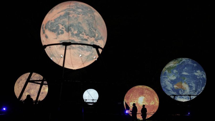 Pengunjung melewati kreasi matahari yang diterangi, kedua kanan, ditampilkan dengan kreasi planet lain termasuk bumi, kanan, di jalur cahaya