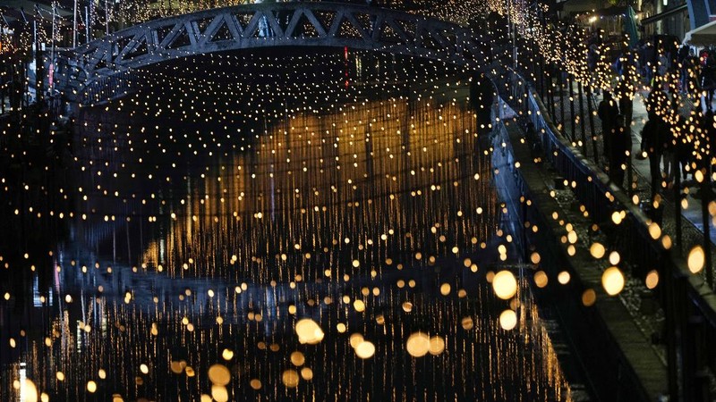 Orang-orang berjalan di jembatan saat lampu Natal menerangi Darsena dei Navigli, lingkungan yang dinamai kanal yang melintasi area Milan, Italia. (AP Photo/Luca Bruno)