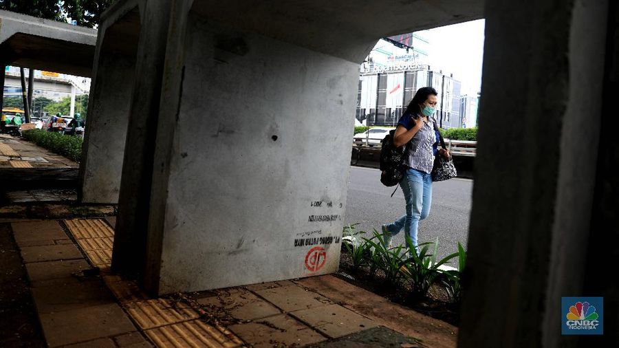 Pejalan kaki melintas di antara material beton saluaran air/gorong-gorong yang berada di jalur pedestrian, kawasan Gatot Subroto, Jakarta, Selasa (21/12). (CNBC Indonesia/Muhammad Sabki)
