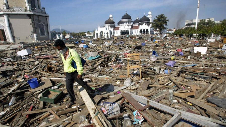 Indonesia Tsunami Mosque as Refuge FILE - In this Dec. 29, 2004 file photo, an Acehnese man walks through debris near the Baiturrahman Grand Mosque in Banda Aceh, about 240 kilometers (150 miles) from the earthquake's epicenter, Indonesia. When the powerful tsunami smashed into this Indonesian city ten years ago, the only structures left standing in many neighborhoods were mosques. For the hundreds who found refuge within their walls, the buildings lifesaving role has not been forgotten - and for many, that experience strengthened their faith. Architectural experts say the mosques in Banda Aceh survived because they were sturdily built and had stronger foundations than surrounding structures, many of which were likely constructed of shoddier materials. But many survivors believe the mosques were spared by divine intervention. (AP Photo/Dita Alangkara, File)