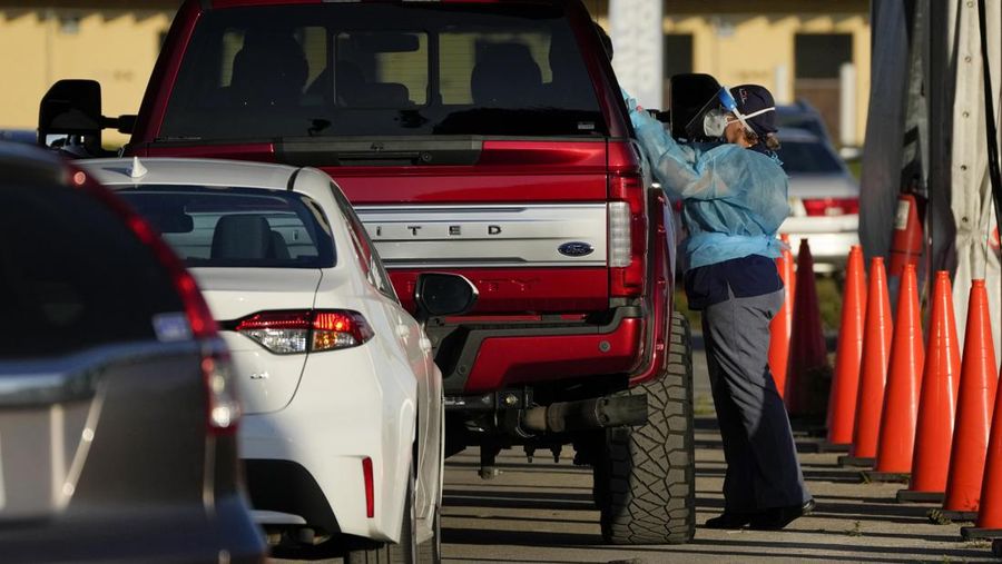 A healthcare worker stands on her toes to test a passenger for COVID-19 at a drive-up testing center at Tropical Park, Wednesday, Dec. 29, 2021, in Miami. (AP Photo/Rebecca Blackwell)