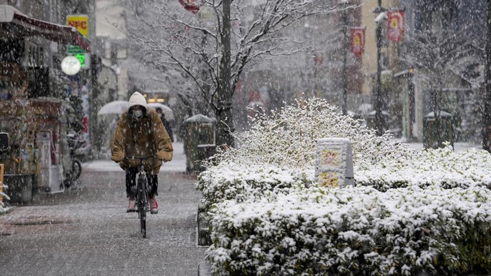 Seseorang mengendarai sepeda saat salju turun di Tokyo, Jepang Kamis (6/1/2022). (AP/Kiichiro Sato)
