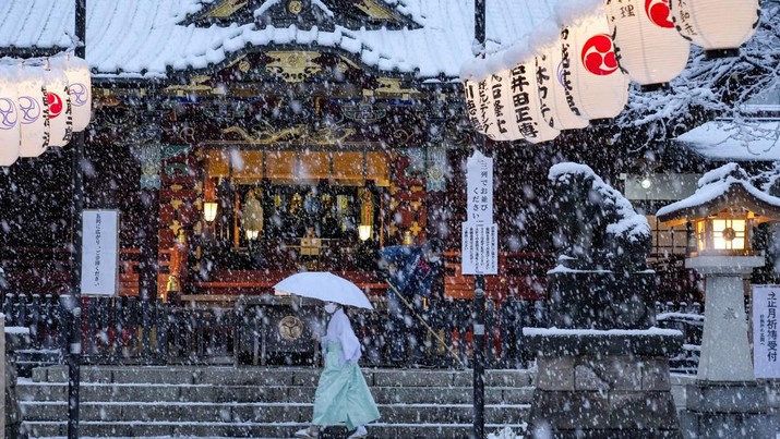 Seorang gadis kuil berjalan melewati kuil utama sementara saat seorang pekerja membersihkan tangga usai salju turun di Tokyo, Jepang Kamis (6/1/2022). (AP Photo/Kiichiro Sato)