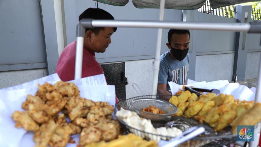 Ira Dijaya (41)melayani pembeli gorengan di kawasan Kebon Jeruk, Jakarta, Jumat (7/1/2022). Berdasarkan Pusat Informasi Harga Pangan Strategis Nasional (PIHPS), secara nasional harga minyak goreng curah pada 29 Desember lalu hanya Rp.18.400/Kg. Pada 6 Januari 2022 atau kemarin, menyentuh Rp. 18.550/Kg, atau naik 0,81%. Kemudian minyak goreng kemasan bermerk 1 pada 30 Desember 2021 harganya Rp. 20.600/Kg. Sementara kemarin menjadi Rp. 20.800/Kg, naik 0,97%. Begitu juga minyak goreng kemasan bermerk 2. Di mana pada 30 Desember masih Rp. 20.030/Kg, kemarin menjadi Rp. 20.300/Kg atau meningkat 1,34%. Harga minyak goreng di pasar tradisional masih tinggi. Pedagang menginginkan harga segera normal kembali. Menurut Ira penjual gorengan 