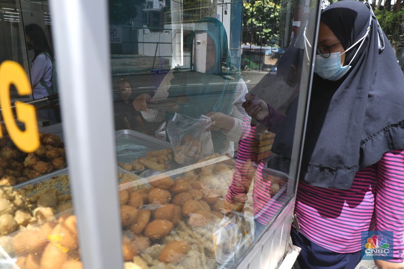 Ira Dijaya (41)melayani pembeli gorengan di kawasan Kebon Jeruk, Jakarta, Jumat (7/1/2022). Berdasarkan Pusat Informasi Harga Pangan Strategis Nasional (PIHPS), secara nasional harga minyak goreng curah pada 29 Desember lalu hanya Rp.18.400/Kg. Pada 6 Januari 2022 atau kemarin, menyentuh Rp. 18.550/Kg, atau naik 0,81%. Kemudian minyak goreng kemasan bermerk 1 pada 30 Desember 2021 harganya Rp. 20.600/Kg. Sementara kemarin menjadi Rp. 20.800/Kg, naik 0,97%. Begitu juga minyak goreng kemasan bermerk 2. Di mana pada 30 Desember masih Rp. 20.030/Kg, kemarin menjadi Rp. 20.300/Kg atau meningkat 1,34%. Harga minyak goreng di pasar tradisional masih tinggi. Pedagang menginginkan harga segera normal kembali. Menurut Ira penjual gorengan 