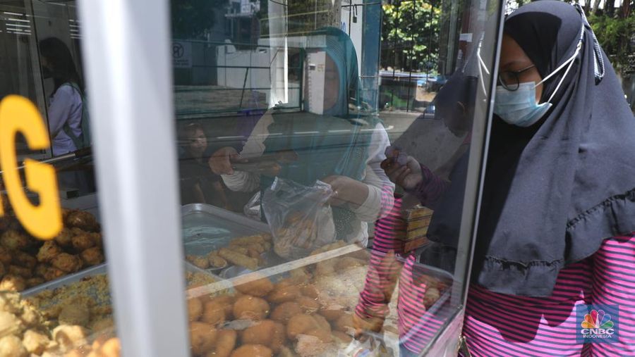 Ira Dijaya (41)melayani pembeli gorengan di kawasan Kebon Jeruk, Jakarta, Jumat (7/1/2022). Berdasarkan Pusat Informasi Harga Pangan Strategis Nasional (PIHPS), secara nasional harga minyak goreng curah pada 29 Desember lalu hanya Rp.18.400/Kg. Pada 6 Januari 2022 atau kemarin, menyentuh Rp. 18.550/Kg, atau naik 0,81%. Kemudian minyak goreng kemasan bermerk 1 pada 30 Desember 2021 harganya Rp. 20.600/Kg. Sementara kemarin menjadi Rp. 20.800/Kg, naik 0,97%. Begitu juga minyak goreng kemasan bermerk 2. Di mana pada 30 Desember masih Rp. 20.030/Kg, kemarin menjadi Rp. 20.300/Kg atau meningkat 1,34%. Harga minyak goreng di pasar tradisional masih tinggi. Pedagang menginginkan harga segera normal kembali. Menurut Ira penjual gorengan 
