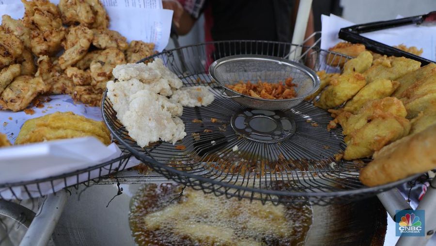 Ira Dijaya (41)melayani pembeli gorengan di kawasan Kebon Jeruk, Jakarta, Jumat (7/1/2022). Berdasarkan Pusat Informasi Harga Pangan Strategis Nasional (PIHPS), secara nasional harga minyak goreng curah pada 29 Desember lalu hanya Rp.18.400/Kg. Pada 6 Januari 2022 atau kemarin, menyentuh Rp. 18.550/Kg, atau naik 0,81%. Kemudian minyak goreng kemasan bermerk 1 pada 30 Desember 2021 harganya Rp. 20.600/Kg. Sementara kemarin menjadi Rp. 20.800/Kg, naik 0,97%. Begitu juga minyak goreng kemasan bermerk 2. Di mana pada 30 Desember masih Rp. 20.030/Kg, kemarin menjadi Rp. 20.300/Kg atau meningkat 1,34%. Harga minyak goreng di pasar tradisional masih tinggi. Pedagang menginginkan harga segera normal kembali. Menurut Ira penjual gorengan 