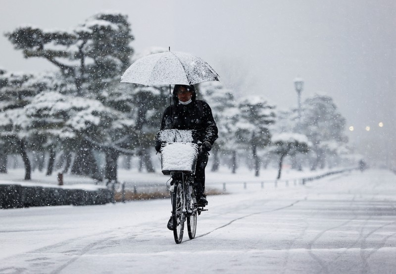 Seseorang mengendarai sepeda saat salju turun di Tokyo, Jepang Kamis (6/1/2022). (AP/Kiichiro Sato)