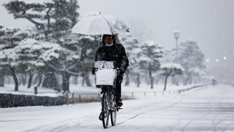 Seseorang mengendarai sepeda saat salju turun di Tokyo, Jepang Kamis (6/1/2022). (AP/Kiichiro Sato)