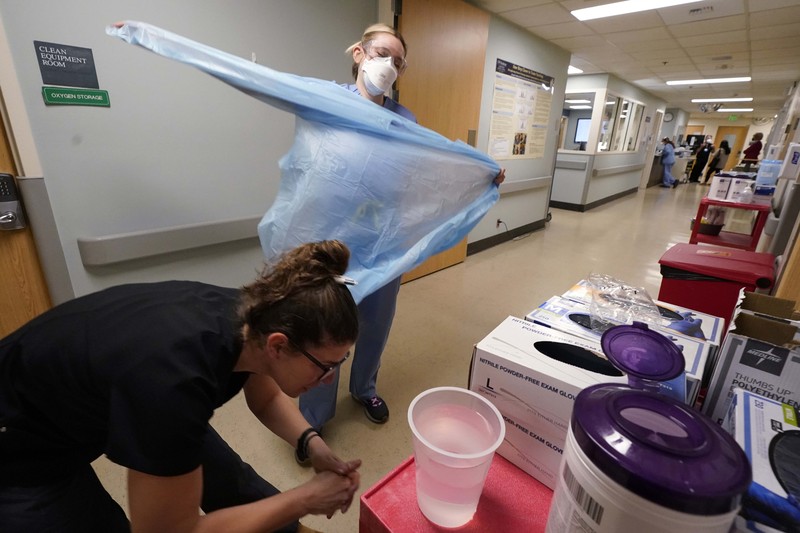 APTOPIX Virus Outbreak Washington Registered nurse Jessalynn Dest, left, removes protective equipment and washes her hands after leaving a COVID-19 patient's room as speech therapist Sam Gibbs puts on safety clothing while preparing to see a patient in the acute care unit of Harborview Medical Center, Friday, Jan. 14, 2022, in Seattle. Washington Gov. Jay Inslee is deploying 100 members of the state National Guard to hospitals across the state amid staff shortages due to an omicron-fueled spike in COVID-19 hospitalizations. Inslee announced Thursday that teams will be deployed to assist four overcrowded emergency departments at hospitals in Everett, Yakima, Wenatchee and Spokane, and that testing teams will be based at hospitals in Olympia, Richland, Seattle and Tacoma. (AP Photo/Elaine Thompson)