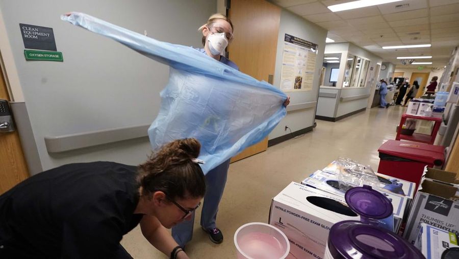 Registered nurse Jessalynn Dest, left, removes protective equipment and washes her hands after leaving a COVID-19 patient's room as speech therapist Sam Gibbs puts on safety clothing while preparing to see a patient in the acute care unit of Harborview Medical Center, Friday, Jan. 14, 2022, in Seattle. Washington Gov. Jay Inslee is deploying 100 members of the state National Guard to hospitals across the state amid staff shortages due to an omicron-fueled spike in COVID-19 hospitalizations. Inslee announced Thursday that teams will be deployed to assist four overcrowded emergency departments at hospitals in Everett, Yakima, Wenatchee and Spokane, and that testing teams will be based at hospitals in Olympia, Richland, Seattle and Tacoma. (AP Photo/Elaine Thompson)
