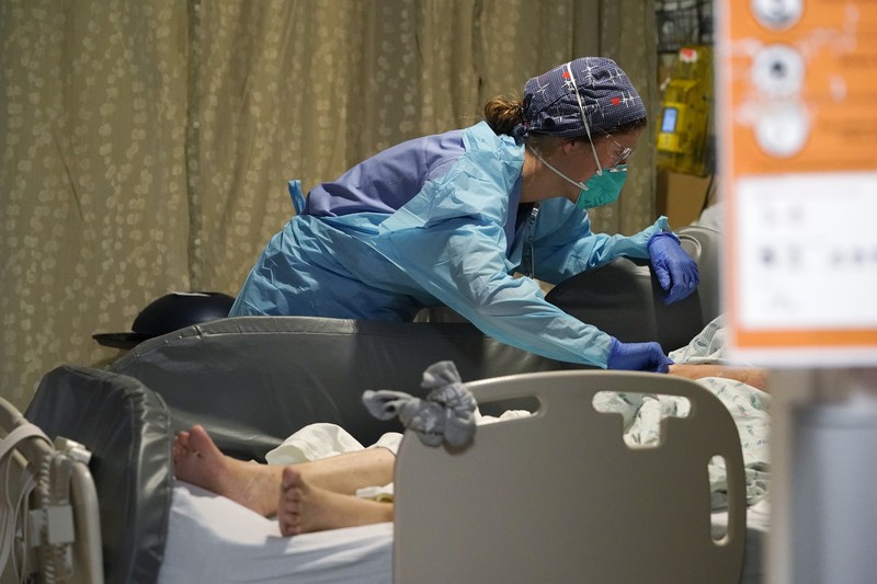 Registered nurse Jessalynn Dest, left, removes protective equipment and washes her hands after leaving a COVID-19 patient's room as speech therapist Sam Gibbs puts on safety clothing while preparing to see a patient in the acute care unit of Harborview Medical Center, Friday, Jan. 14, 2022, in Seattle. Washington Gov. Jay Inslee is deploying 100 members of the state National Guard to hospitals across the state amid staff shortages due to an omicron-fueled spike in COVID-19 hospitalizations. Inslee announced Thursday that teams will be deployed to assist four overcrowded emergency departments at hospitals in Everett, Yakima, Wenatchee and Spokane, and that testing teams will be based at hospitals in Olympia, Richland, Seattle and Tacoma. (AP Photo/Elaine Thompson)