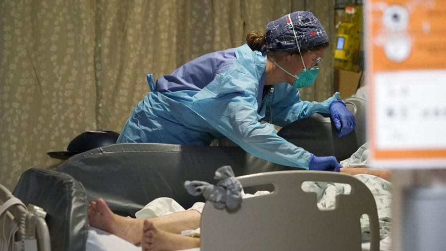Registered nurse Estella Wilmarth tends to a patient in the acute care unit of Harborview Medical Center, Friday, Jan. 14, 2022, in Seattle. Washington Gov. Jay Inslee is deploying 100 members of the state National Guard to hospitals across the state amid staff shortages due to an omicron-fueled spike in COVID-19 hospitalizations. Inslee announced Thursday that teams will be deployed to assist four overcrowded emergency departments at hospitals in Everett, Yakima, Wenatchee and Spokane, and that testing teams will be based at hospitals in Olympia, Richland, Seattle and Tacoma. (AP Photo/Elaine Thompson)