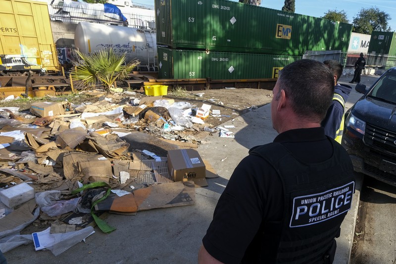 Pekerja kontraktor Adam Rodriguez (depan) dan Luis Rosas mengambil ban kendaraan dari kotak dan paket yang robek di sepanjang bagian rel kereta Union Pacific di pusat kota Los Angeles Jumat (14/1/2022).  Pencuri telah merampok kontainer kargo di atas kereta dekat pusat kota Los Angeles selama berbulan-bulan dan juga mereka meninggalkan ratusan kardus dan barang-barang yang menurut para pencuri tidak cukup berharga untuk diambil. (AP/Ringo H.W. Chiu)