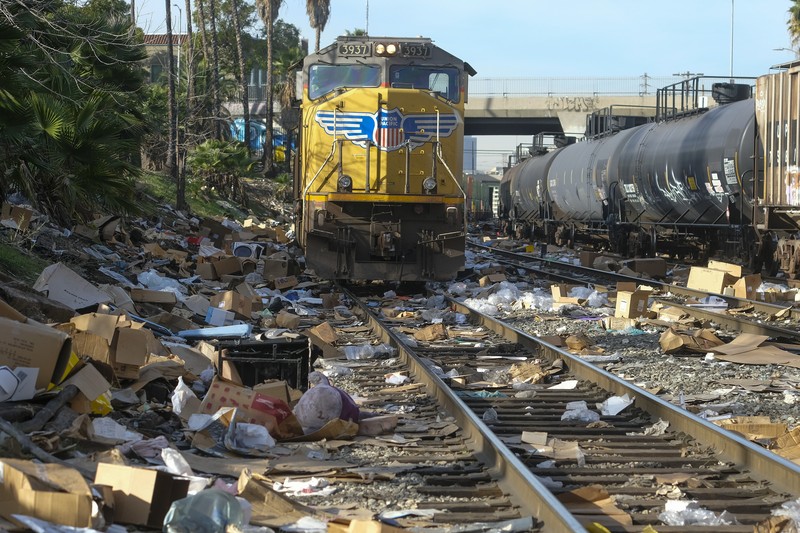 Pekerja kontraktor Adam Rodriguez (depan) dan Luis Rosas mengambil ban kendaraan dari kotak dan paket yang robek di sepanjang bagian rel kereta Union Pacific di pusat kota Los Angeles Jumat (14/1/2022).  Pencuri telah merampok kontainer kargo di atas kereta dekat pusat kota Los Angeles selama berbulan-bulan dan juga mereka meninggalkan ratusan kardus dan barang-barang yang menurut para pencuri tidak cukup berharga untuk diambil. (AP/Ringo H.W. Chiu)